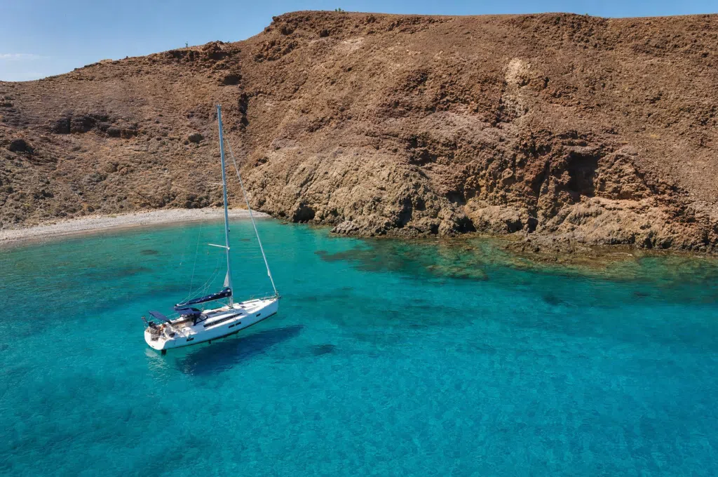 En sejlyacht ankret op i en turkisbugt under brune vulkanske klipper ud for Gran Canarias sydkyst